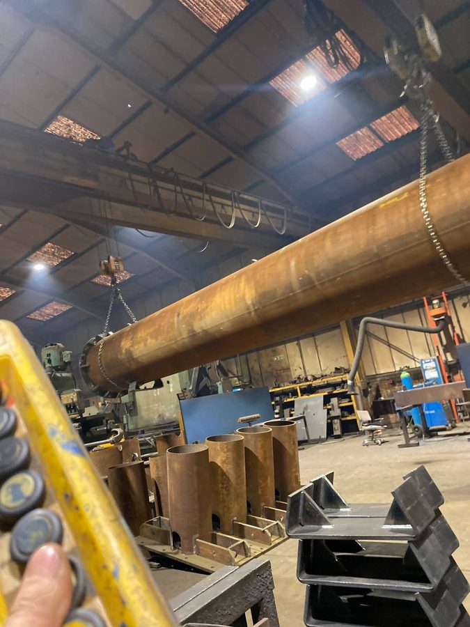Overhead crane lifting a fabricated pipe section in an engineering workshop